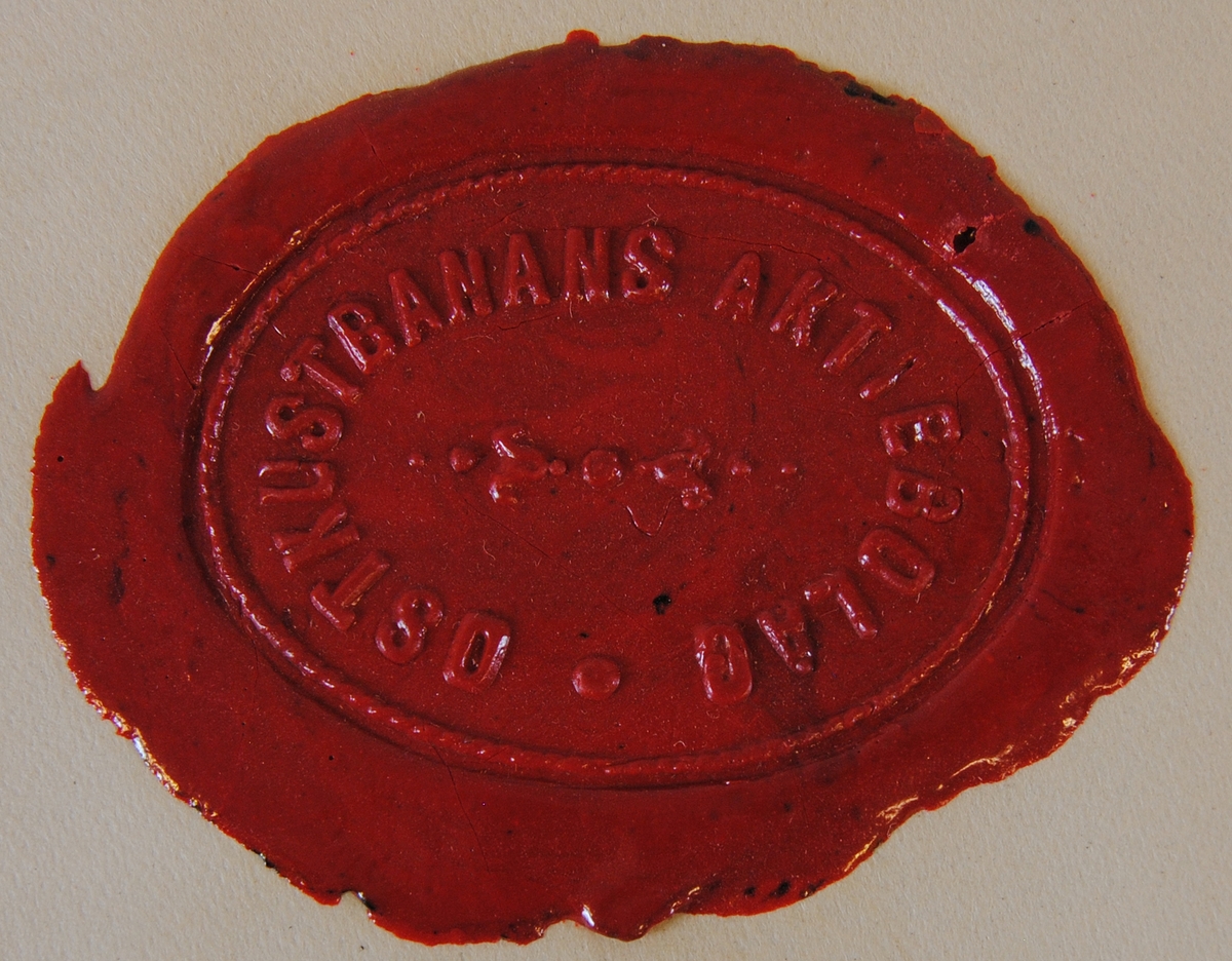 Ovalt sigillavtryck i rött lack på gultonat papper. Texten löper längs ovalens ytterkant och i mitten finns ett ornament i form av stiliserade liljor.