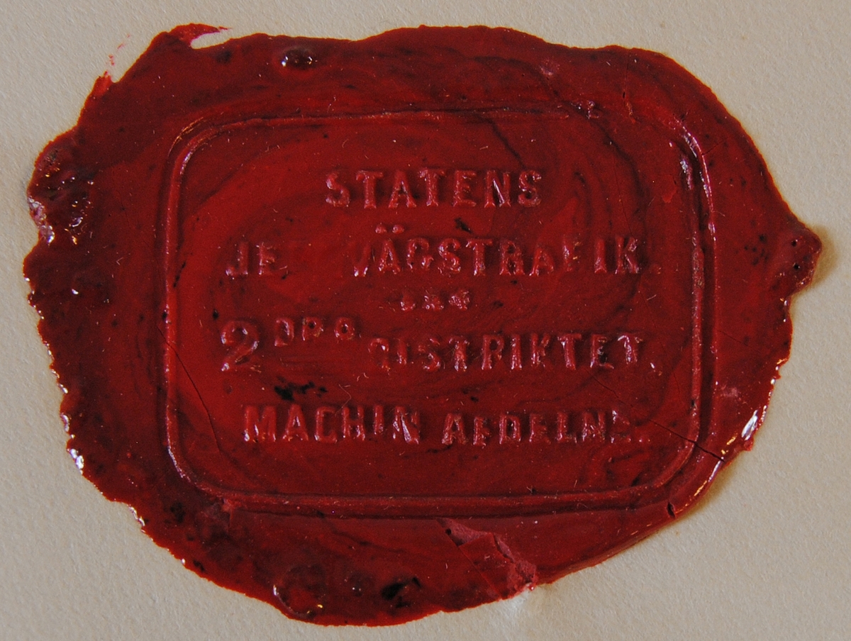 Rektangulärt sigillavtryck med rundade hörn i rött lack på gultonat papper. Texten löper över fyra rader med ett litet ornament i mitten.