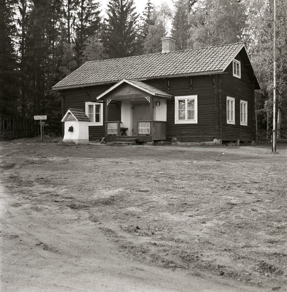 Sockenstygan i Hembygdsbyn har dekorerad förstukvist, tegeltak, skorsten, gärdesgård och flaggstång, 1975.