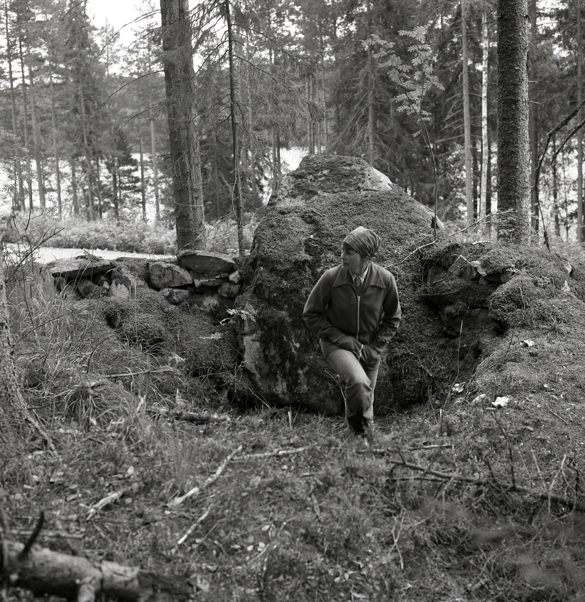 En kvinna står i en grop intill en stor sten i skogen. Bilden är tagen i samband med invigningen av en kyrkstig vid Tannåsen, september 1977.