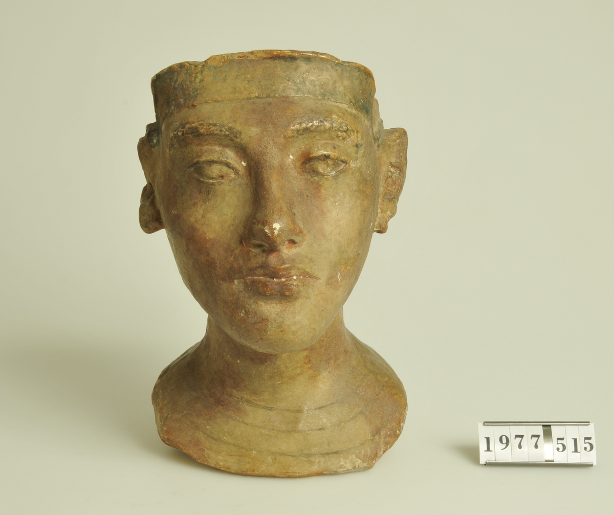 Huvud av keramik med glasyr i rött och svart.
Troligen kopia av egyptiskt gravfynd.
Stämpel: I botten en mässingsplatta med text:
"FELIX NANNES MÃœNCHEN".

