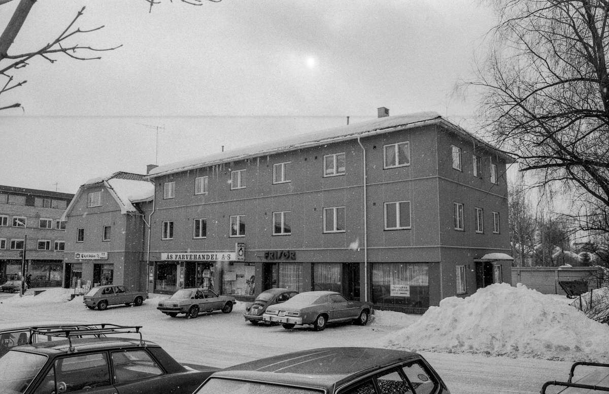Skoleveien 1 i Ås skal bli legesenter. Vinterbilde med parkerte biler utenfor, stor snøhaug. Murbygninger i Ås sentrum.