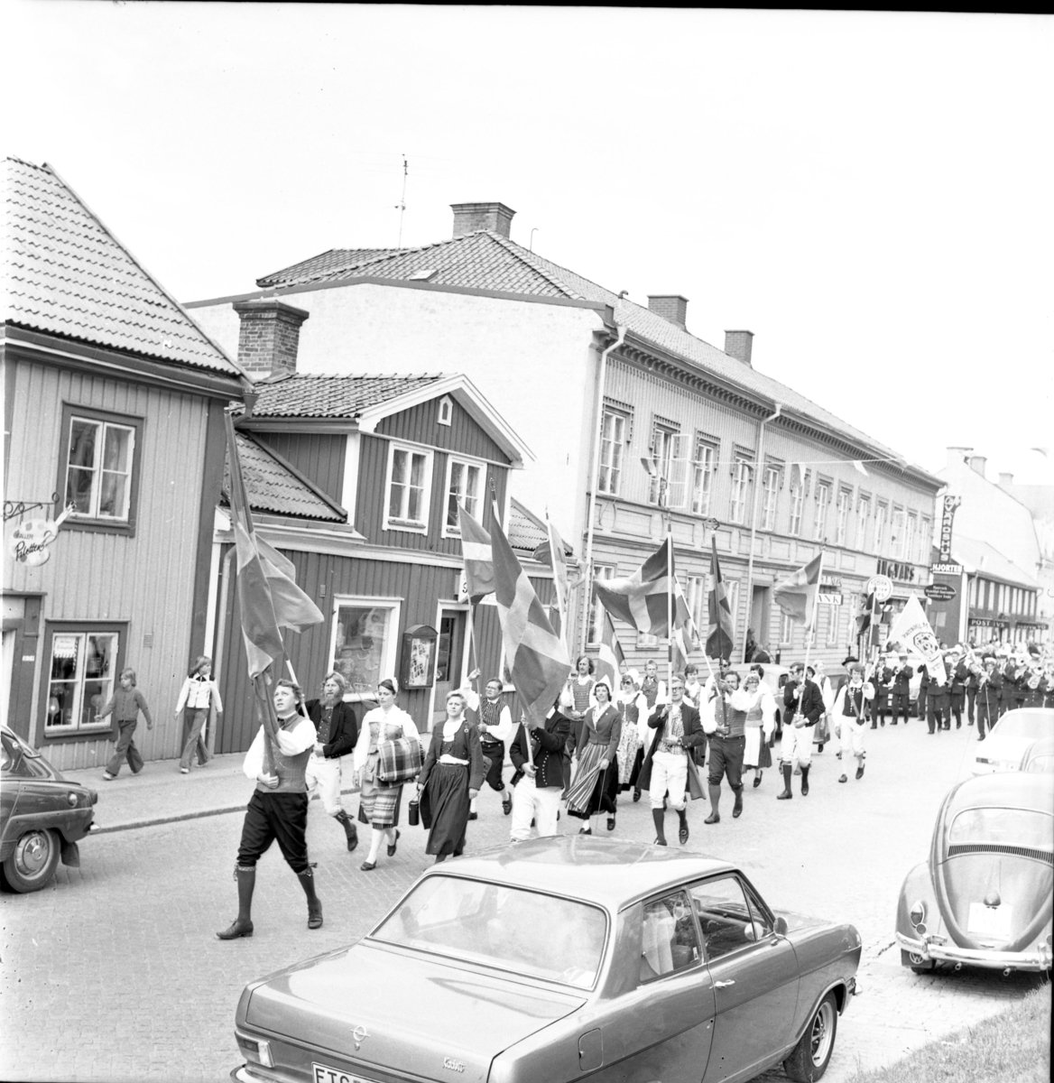 Musikkår med fanborg i täten och folkdansare på slutet marscherar på Brahegatan. I samband med Grännapolkan på Grännaberget, 1975.