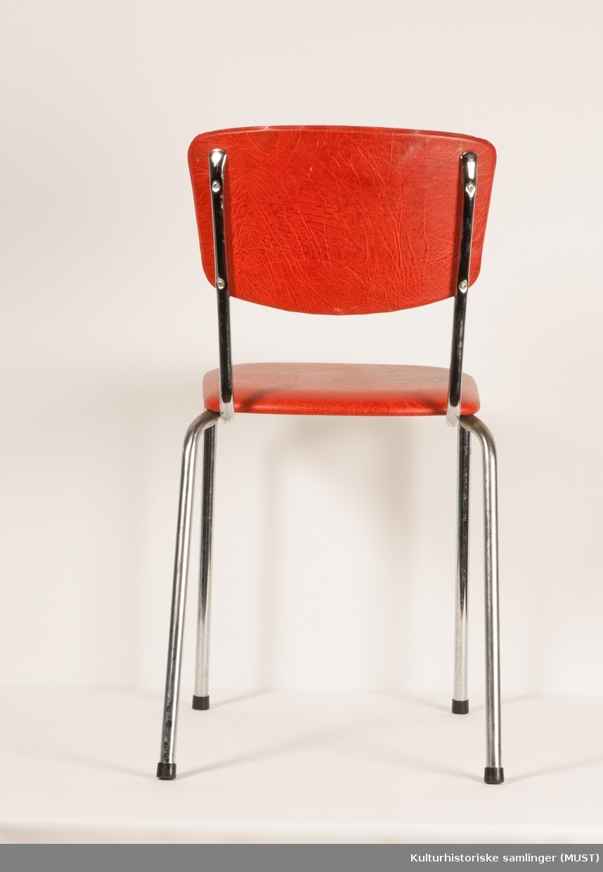 Stålrørsstol, trukket med rød skai i sete og rygg. 
Produsert på Norsy, i Førresfjorden.