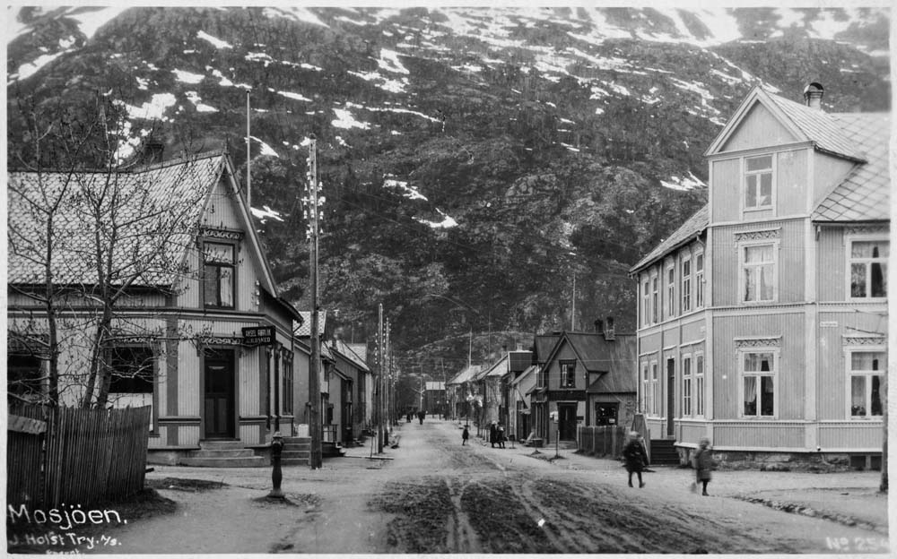 Postkort med motiv av krysset mellom Kirkegata og Peter Bechs gate i Mosjøen. Aksel Rørvik Guldsmed til venstre.
