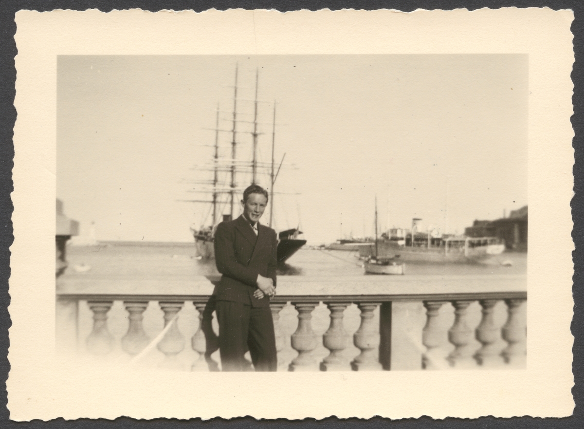 Porträtt av Evert Ingemansson i kostym som står vid en balustrad i Monte Carlo. I bakgrunden syns yachten Sea Cloud