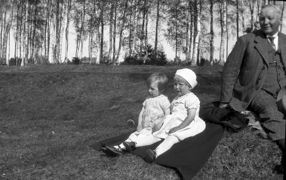Mann og to småjenter sitter på bakken.