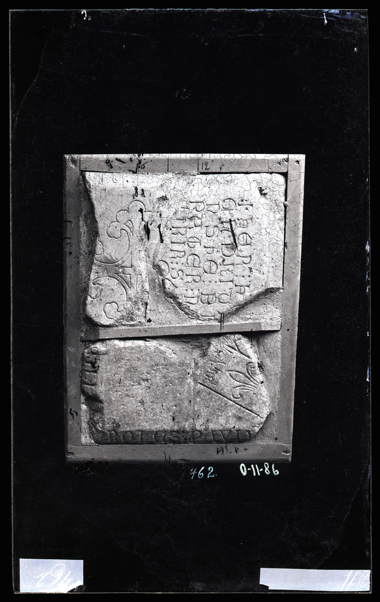 Deler av to gravsteiner fra middelalder (ca. 1300-tallet) fra Nidarosdomen. 

Øverste stein er dekorert med et liljekors. 

Nederste stein har en lilje og delvis tekst på latin: ... BILI : PROLES : PAVLV

"Nobilium proles Paulus" - Pål av adel ætt

Nederste stein er et fragment av en større gravstein, og står utstilt i Nidarosdomens gravsteinsutstilling (stein nummer 19). 