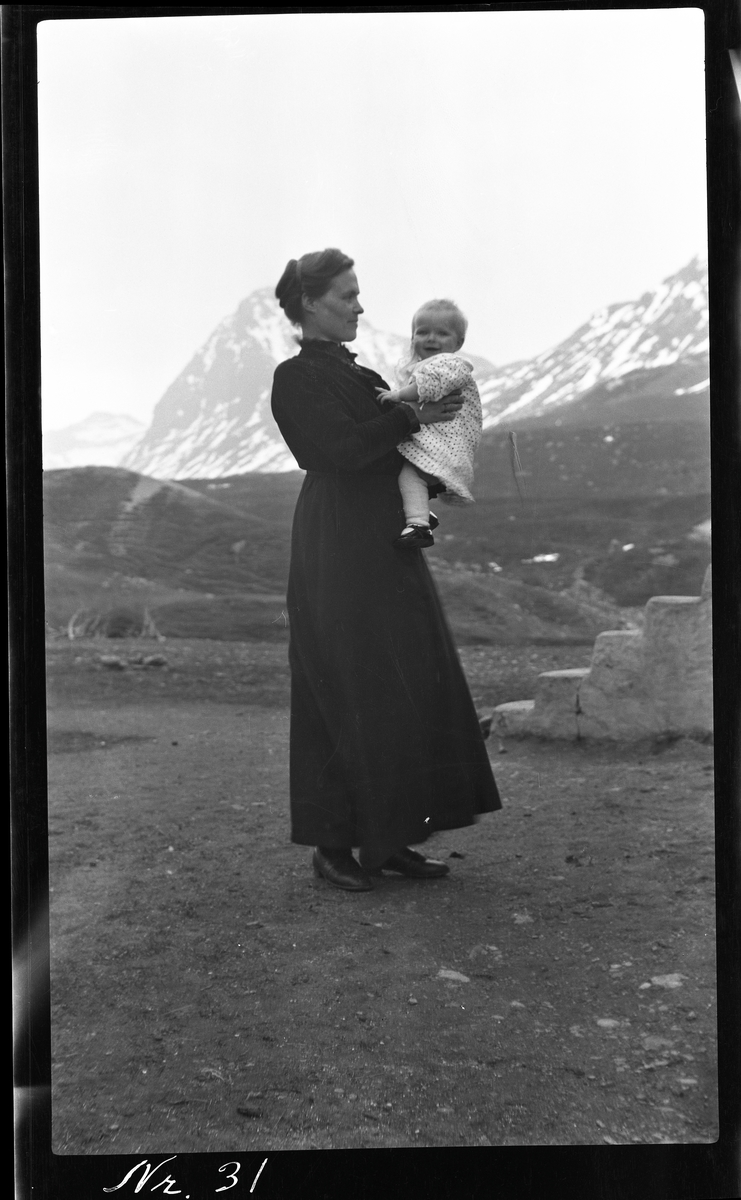 Portrett av kvinne med barn, fotografert utendørs med fjell i bakgrunnen.