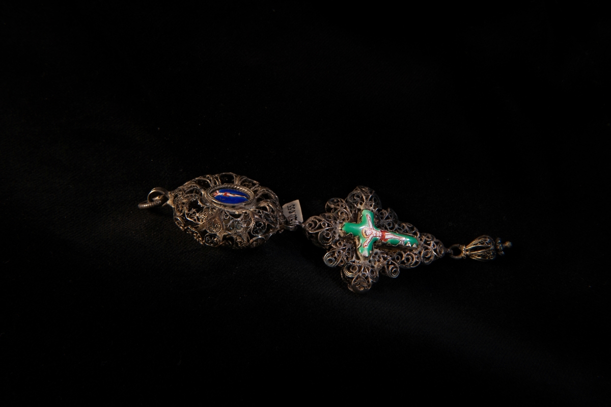 Ett hängsmycke av filigran, bestående av en rundel med kors under, prydda med polykrom religiös emaljdekor med Jesus på korset, Veronikas svetteduk m.m. i grönt blått, rött och vitt. Kedja saknas.