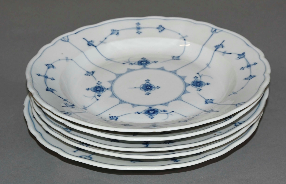 Fem tallerkener av glassert keramikk, med blåfarget dekormaling.