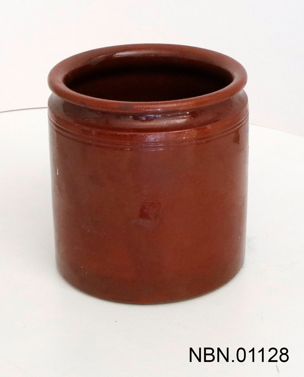 Sylinderformet krukke. Rødbrun keramikk, glasert på inn- og utsiden. To riller parallelt med munningskanten på utsiden, samt en bred rille over dette.