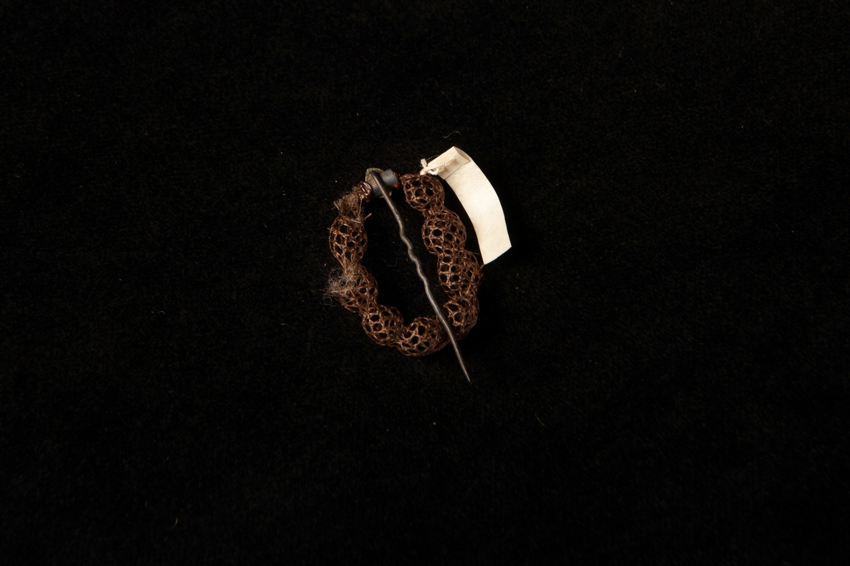 Schalnål i form av en brun, oval ring i hårarbete.