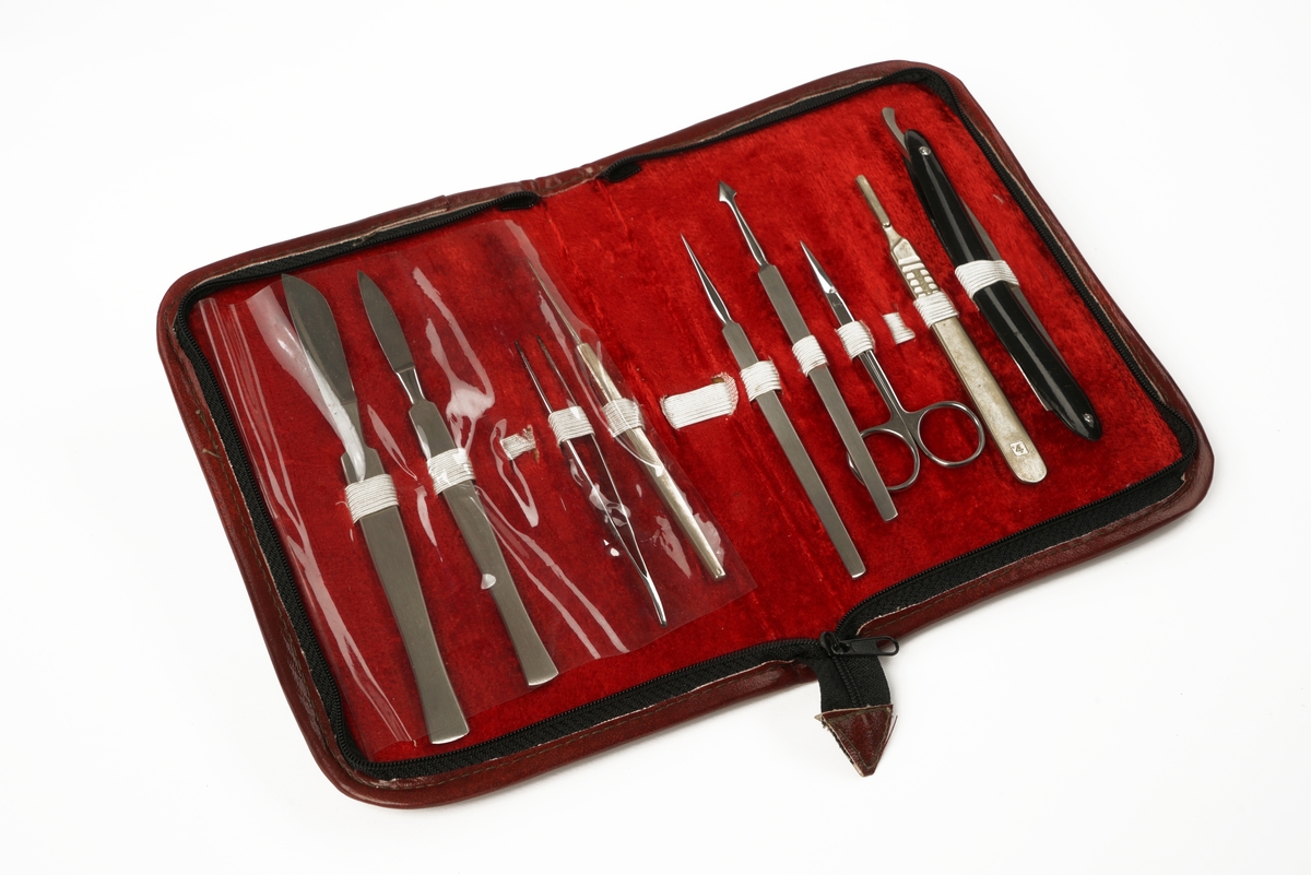 Etui som brettes dobbelt og lukkes med glidelås inneholdende ulike typer verktøy: to typer skalpeller, tre typer nåler, pinsett, barberkniv, knivbladholder og saks.