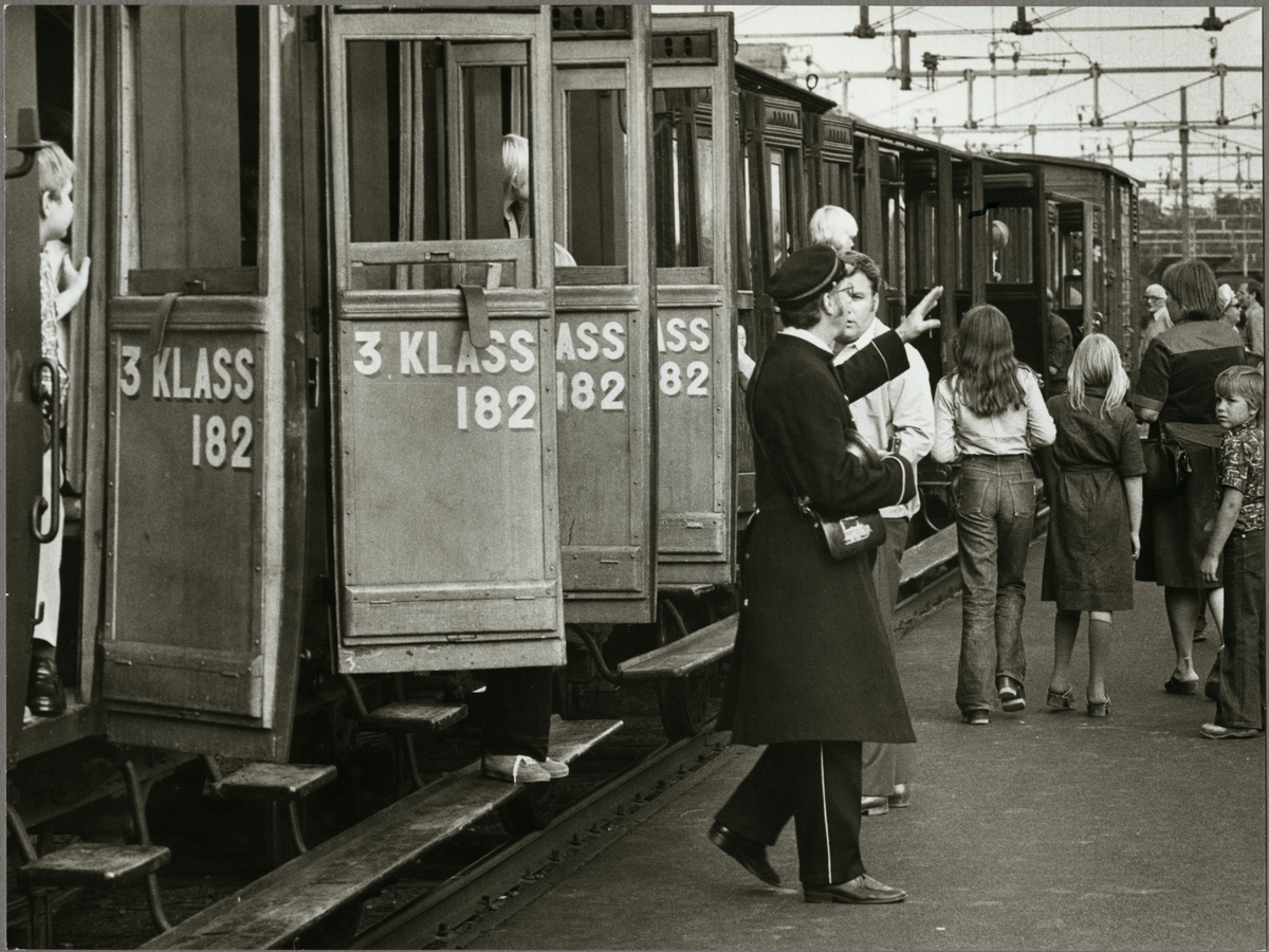 Konduktör och passagerare vid ett persontåg med vagnar av äldre modell.