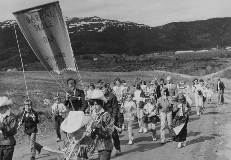Leirfjord, Bardal. 17.mai-tog med fane fra Bardal skole. Korpsmusikk og glade barn med flagg, bunad og fine klær.
Pressebilde fra Helgeland arbeiderblad.