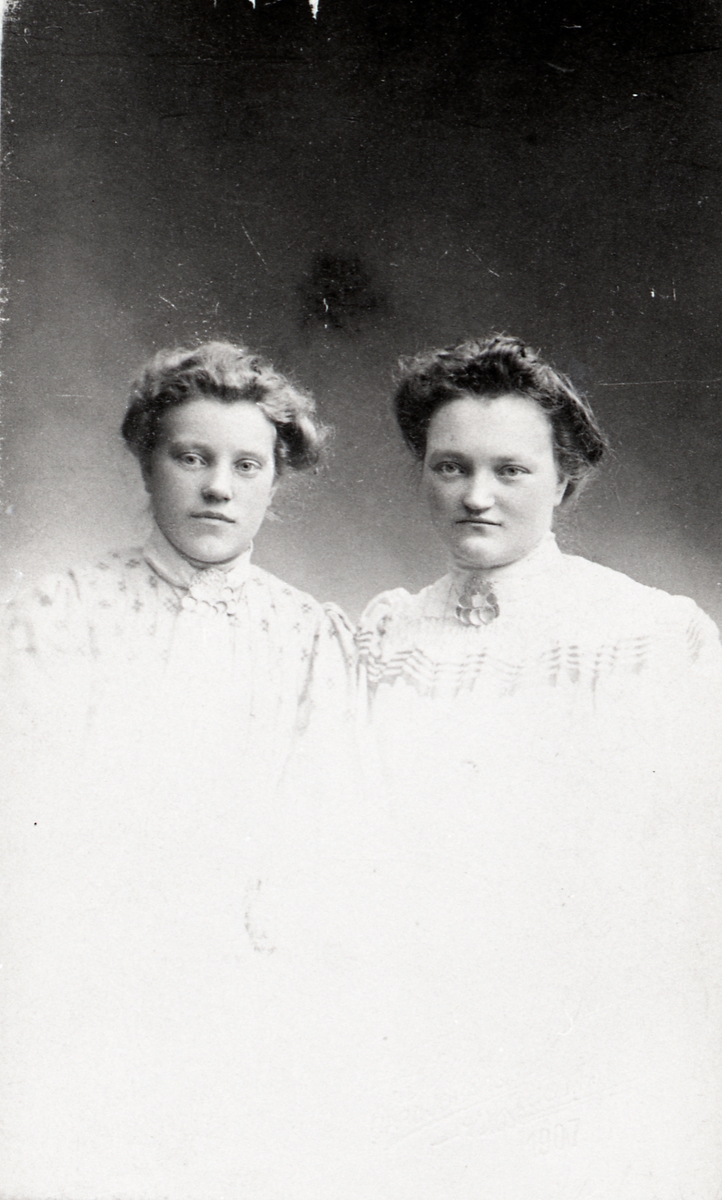 Portrett av to kvinner. Dei er begge kledde i kvite blusar og begge har ei sølje i halsen.