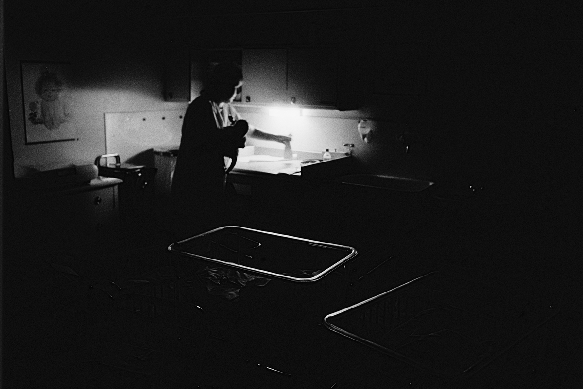 Nattsköterska sköter om ett spädbarn i barnsalen, lättvårdsavdelningen Ringblomman, Gillbergska barnhemmet, Sysslomansgatan 37 - 39, Uppsala 1986