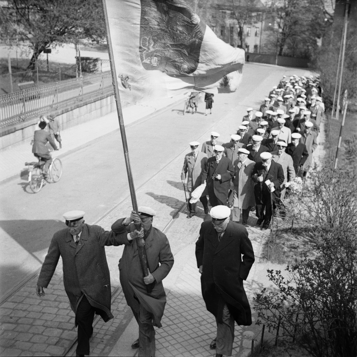 Flera personer iförda studentmössor tågar tillsammans längs med Biskopsgatan, Östgöta nations minneslandskap, Uppsala 1949
