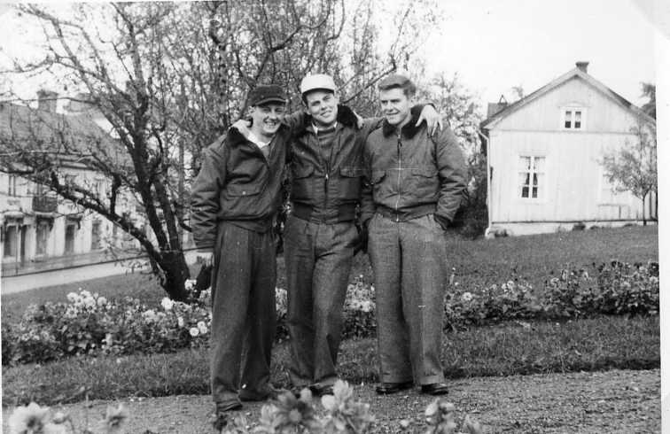 Tre glada unga män i flygarjackor och keps på huvudet står i Andréeparken i Gränna, nuvarande Braheparken, med Franckska gården i bakgrunden. Till vänster skymtar Brahegatan 37.