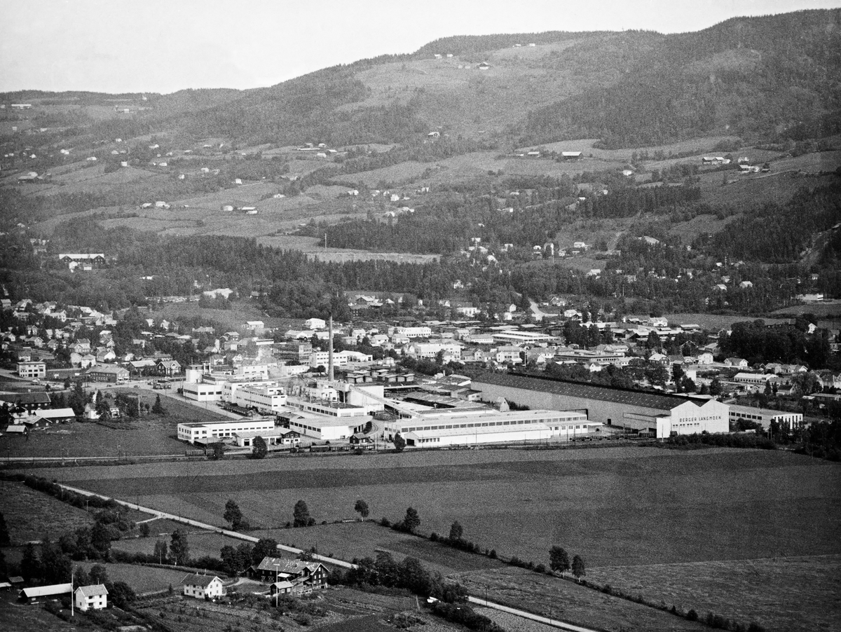 Flyfotografi (svart-hvit papirkopi) tatt fra vest av hjørnesteinsbedriften Berger Langmoen i Brumununddal, Ringsaker kommune, Hedmark fylke. Bildet er sannsynligvis tatt i 1962/1963.  Her ser vi blant annet parkettfabrikken som ligger på Veldre-sida av elva Brumunda, altså til høyre ibildet. Parkettfabrikken ble etabblert i 1962/1963. I forgrunnen på bildet ser vi det nye høvleriet. Det store bygget med navnet Berger Langmoen på gavlveggen var lagerbygg for trelast.  Landbruksproduksjonen på småbruket Strand (i forgrunnen) og garden Granerud (med tun til venstre i bildet) ble etter hvert eksponert for et betydelig arealpress fra den industrielle aktiviteten.  I bakgrunnen skimter vi noe av kulturlandskapet i Nordåsen.