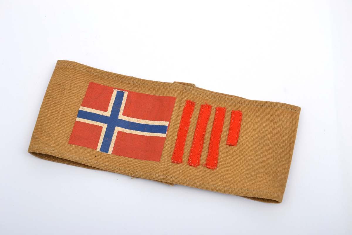 Armbind framstilt i brunt, grovt lerreetsstoff med det norske flagg og fire smale striper.