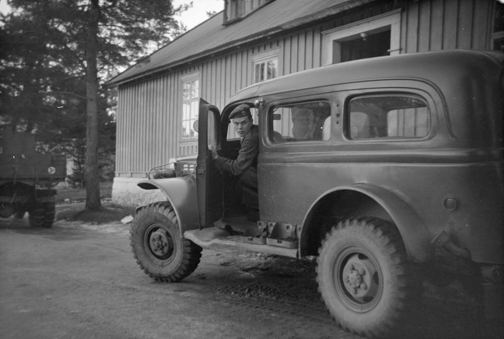 Soldat i bil utenfor hus. Dodge "kvarting" (3/4 tonner), Dodge WC 53 Carryall, under rygging.