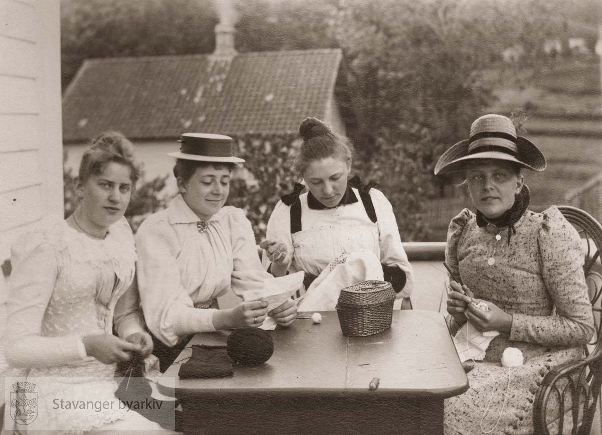 Fire kvinner med strikketøy sitter ved bordet på altanen.