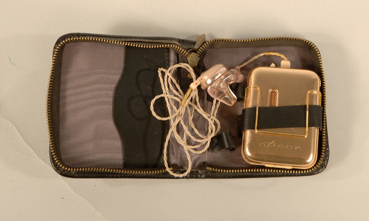Høreapparat med svart skinnveske med glidelås. Gullfarget batteri beholder, plast apparat. Komplett.