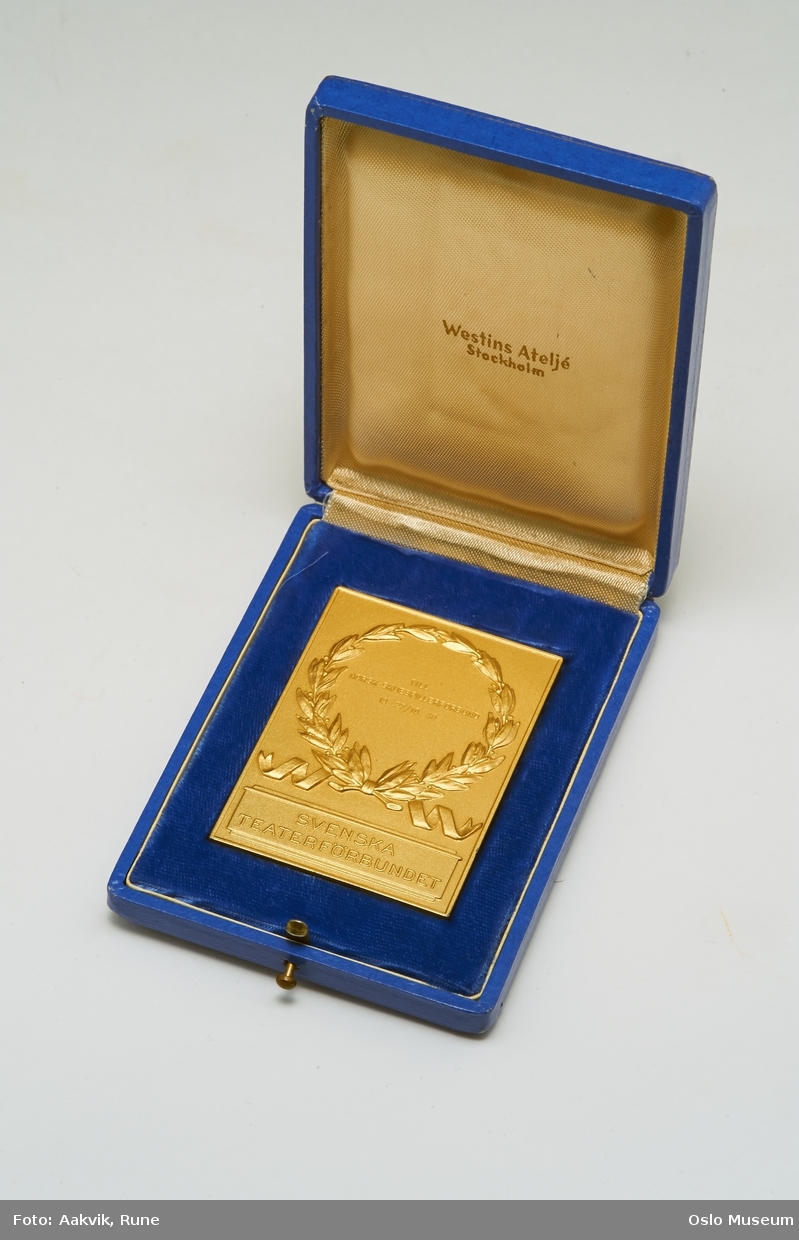 Laubærkrans støpt in relieff på medaljongen, tekst under