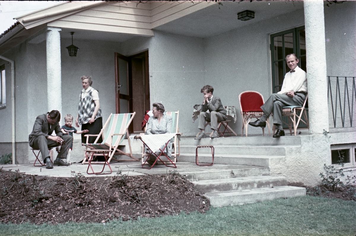 Fra verandaen på en villa i Askim juni 1957. Til høyre sitter Paul Evensen som var gift med Ingeborg født Huset. De øvrige personene fra venstre: Kjell Røisli, Geir Huset, Sigrun Huset (f.Røisli), Karine Røisli, og Stein Evensen, Paul og Ingeborg Evensens sønn.