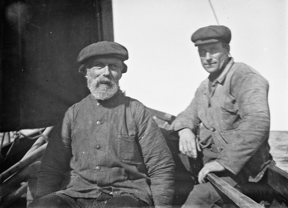Leirfjord, Ulvangen. Nikolai Nilsen Ulvang og Adolf ? i fiskebåt med seil. Begge i arbeidstøy med sixpence på hodet.