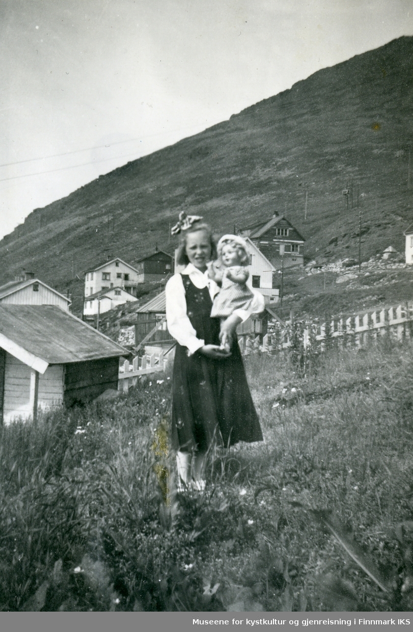 Honningsvåg. Berit Grøtta med sin dukke. Gjenreisningsbebyggelse i bakgrunnen. Ca. 1954.