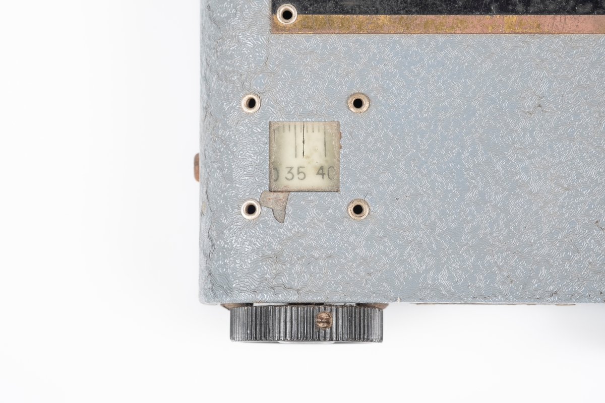 En kortbølgeradio med ytterplater er av metall som er lakkert i grått. Radioen har to svarte vriknapper. Det er et lite vindu ved den ene vriknappen som viser frekvensen. På baksiden er det ledning som kobles til batteriet. Det er to hull til plugger og en kontakt for øreproppene. Det er påfestet en plate med instrukser på på oversiden. Mellom vriknappene er det påfestet en liten plate med modellnummer.