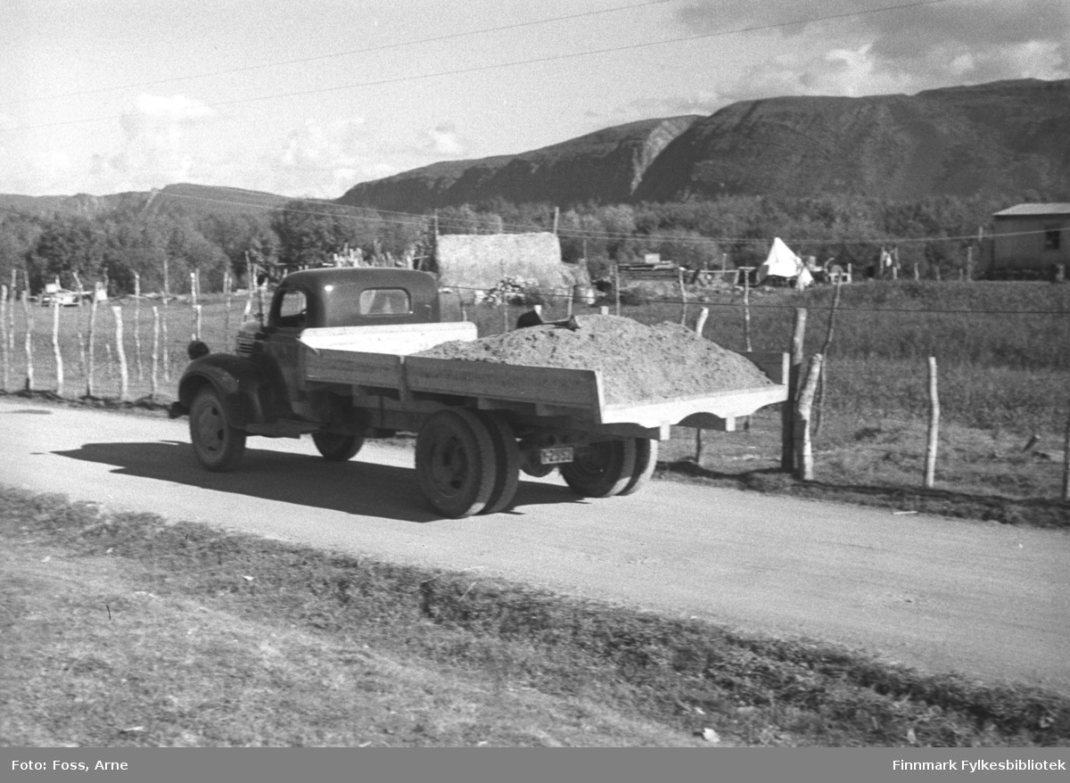 En lastebil kjører langs veien i Bonakas i Tana i august-september 1946. Vi ser mot Blåberget, Rødberget og Austertana bak der. Lastebilen har reg.nr. Y-2552 og er en Dodge eller Fargo 1946-47-modell.