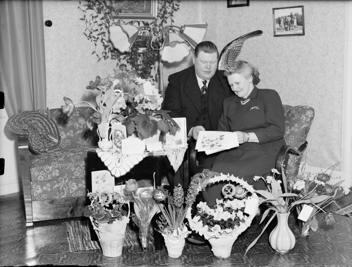 Kvinna och man i hemmiljö omgiven av blommor, Östhammar, Uppland,