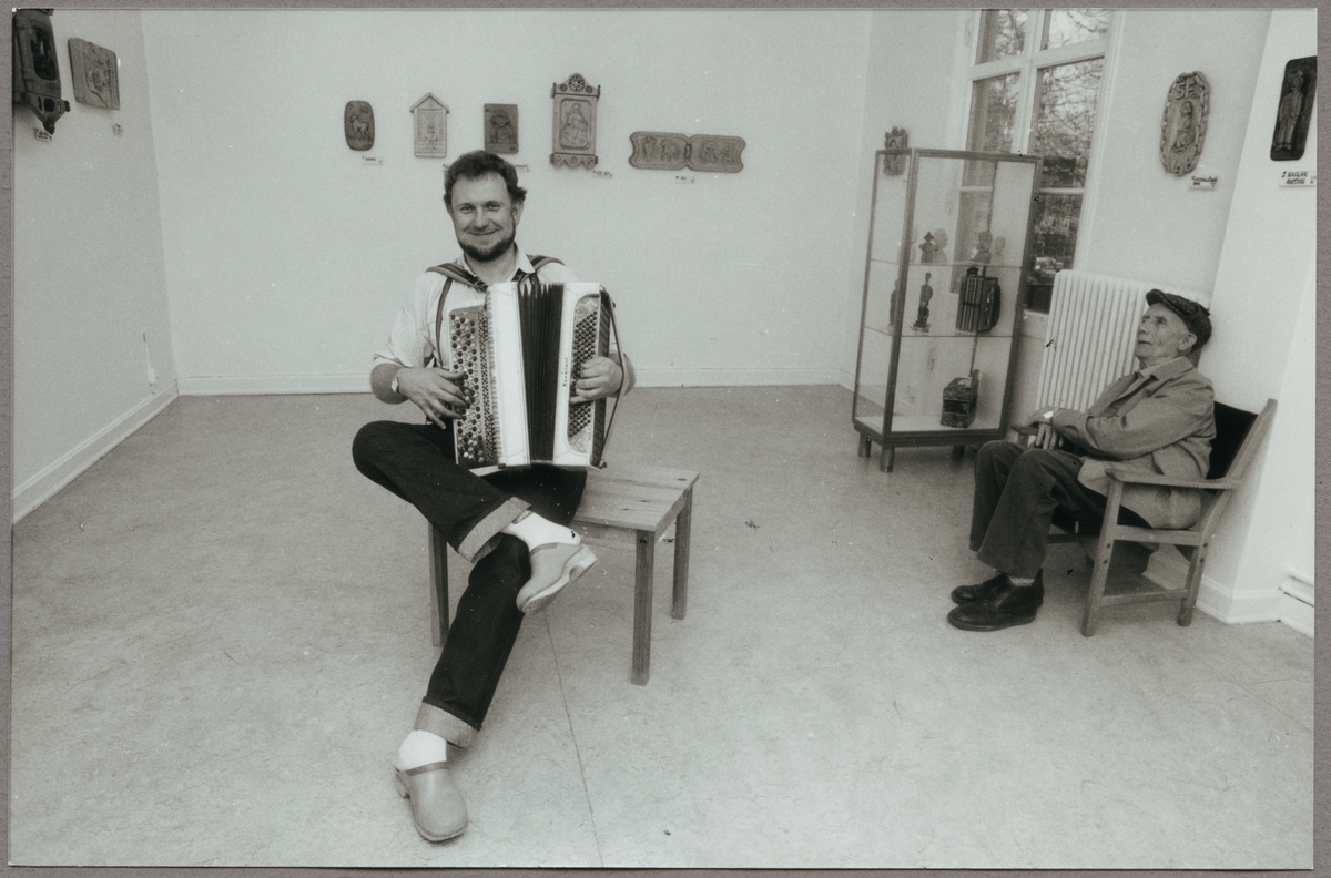 Håkan Carlsson vid dragspelet under en utställning av sina verk med en åhörare 1987.