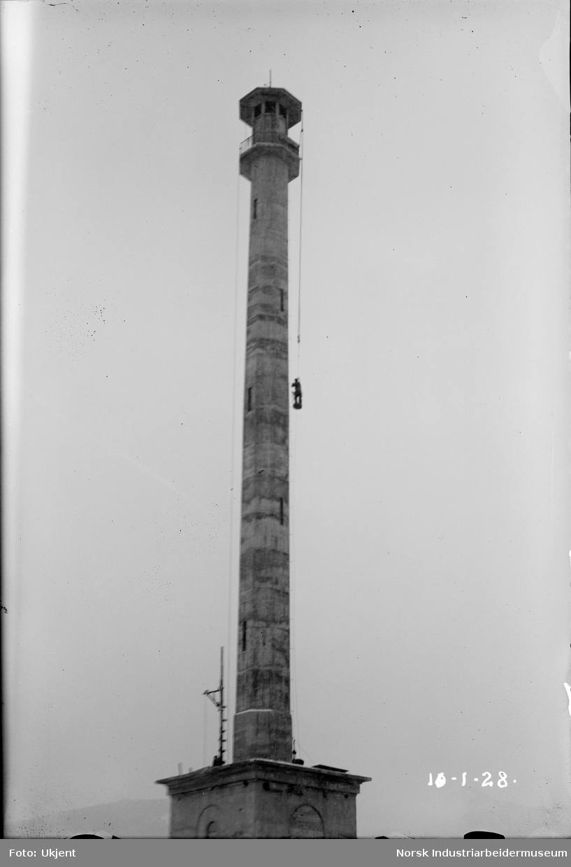 Utvendige arbeider på Hydrotårnet ("Minareten"). Mann henger i tau fra toppen og utfører arbeid.