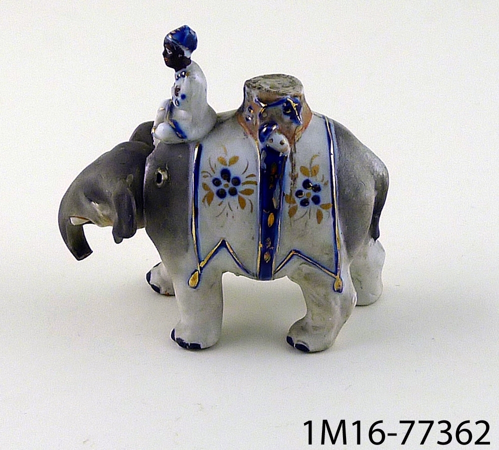 Tvådelad figur i porslin föreställande elefant med elefantförare. Figuren ser ut att ha varit konstruerad så att elefanthuvudet varit rörligt.
