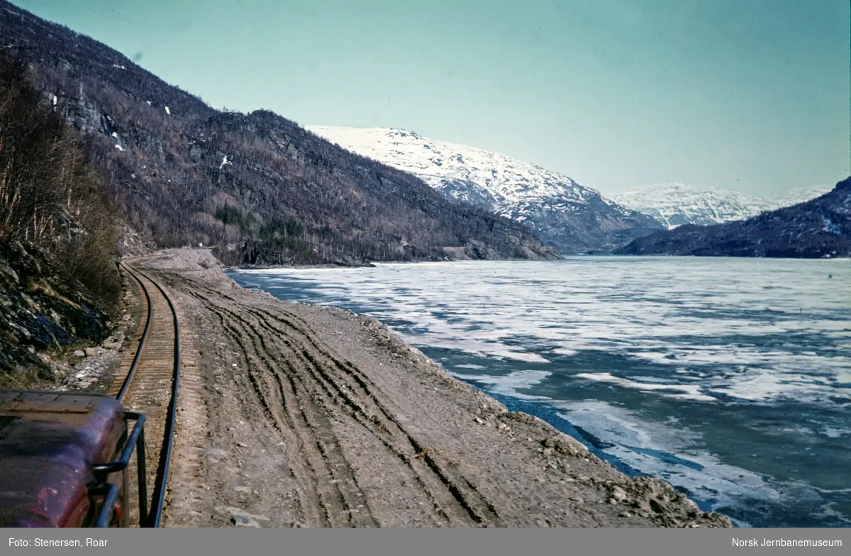Ved Langvatnet, underveis fra Finneid til Lomi med blandet tog, i førerrommet på Sulitjelmabanens diesellokomotiv Odin.Arbeid med bygging av vei som erstatning for jernbanen pågår for fullt.