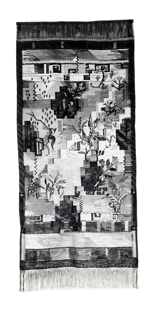Foto (svart/vitt) av en bonad i haute-lisse med stiliserat växtmönster m.m.
Inskrivet i huvudbok 1983.