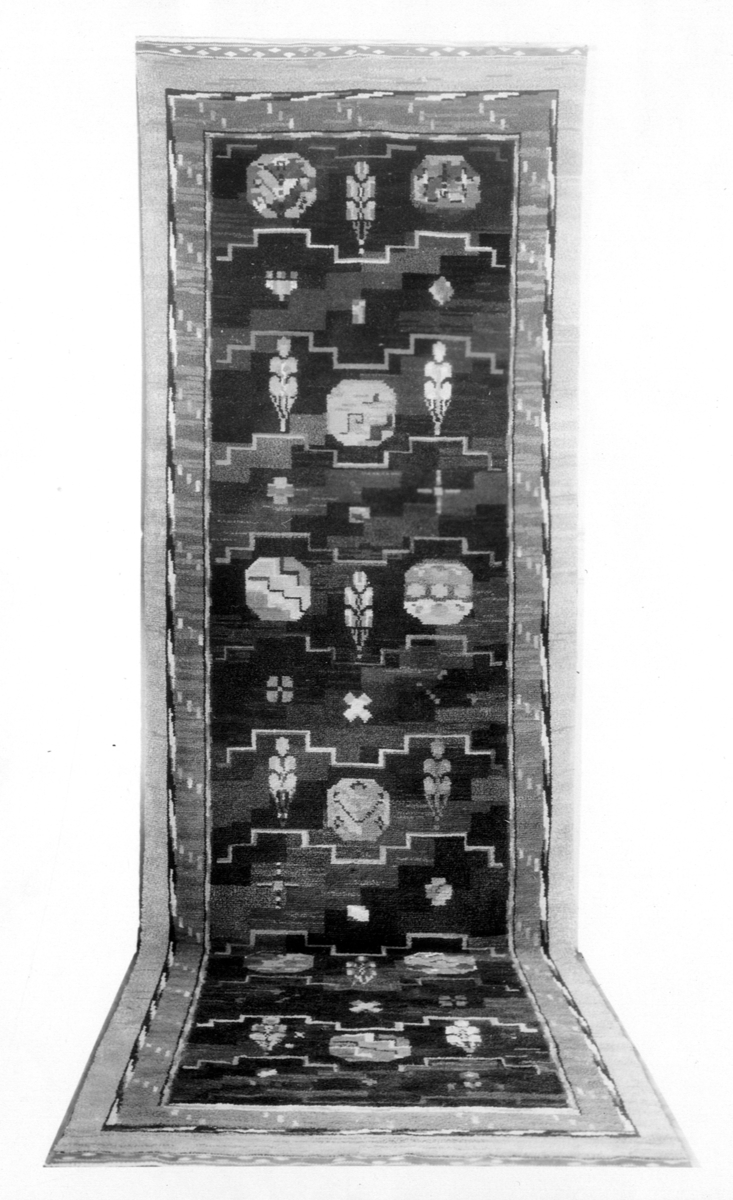 Foto (svart/vitt) av en flossamatta med geometriskt mönster, blandat med stiliserade blommotiv. Beställd och utförd för Svenska Amerika-linjens m/s "Kungsholm". 

Inskrivet i huvudbok 1983.