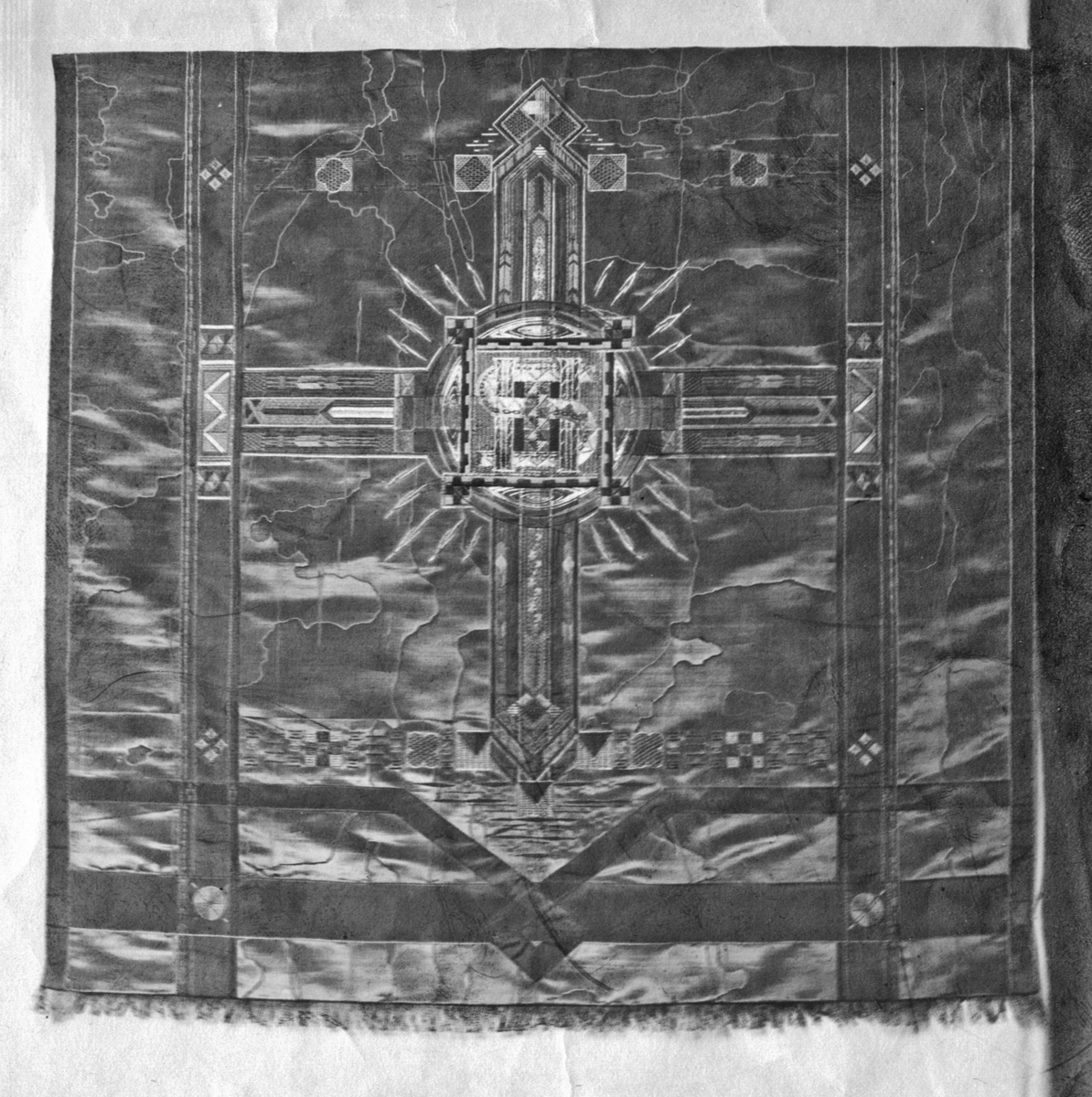 Foto (svart/vitt) av en kalkduk (?) i mörkt vattrat siden, broderad med metalltråd. I mitten en fyrkant, med ett stort "S" i mitten. 

Inskrivet i huvudbok 1983.