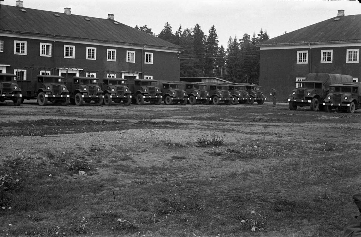 Avfotografert bilde av en rekke militære kjøretøy oppstilt foran bygninger, trolig i en militærleir.