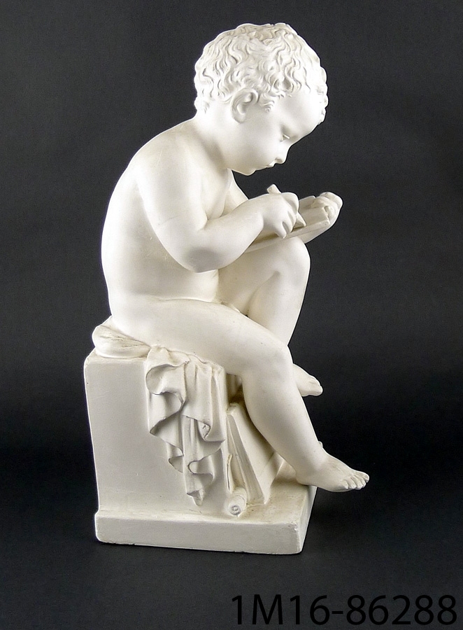 Figur av vit gips, föreställande sittande skrivande pojke.
