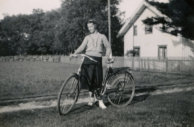 Inga Lill Svensson står med sin cykel vid en grusväg cirka 1930 - 40. Hon var sommagäst till "Högsåkerns", "Aronssons" Sporred 1:5 .