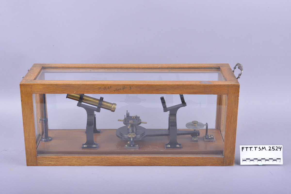 En sekstant i overbygd glassboks, bestående av delene til sekstanten festet på en treplate med formål å vise de forskjellige delenes funksjoner. Glassboksen har en ramme av treverk og et håndtak i den ene enden.