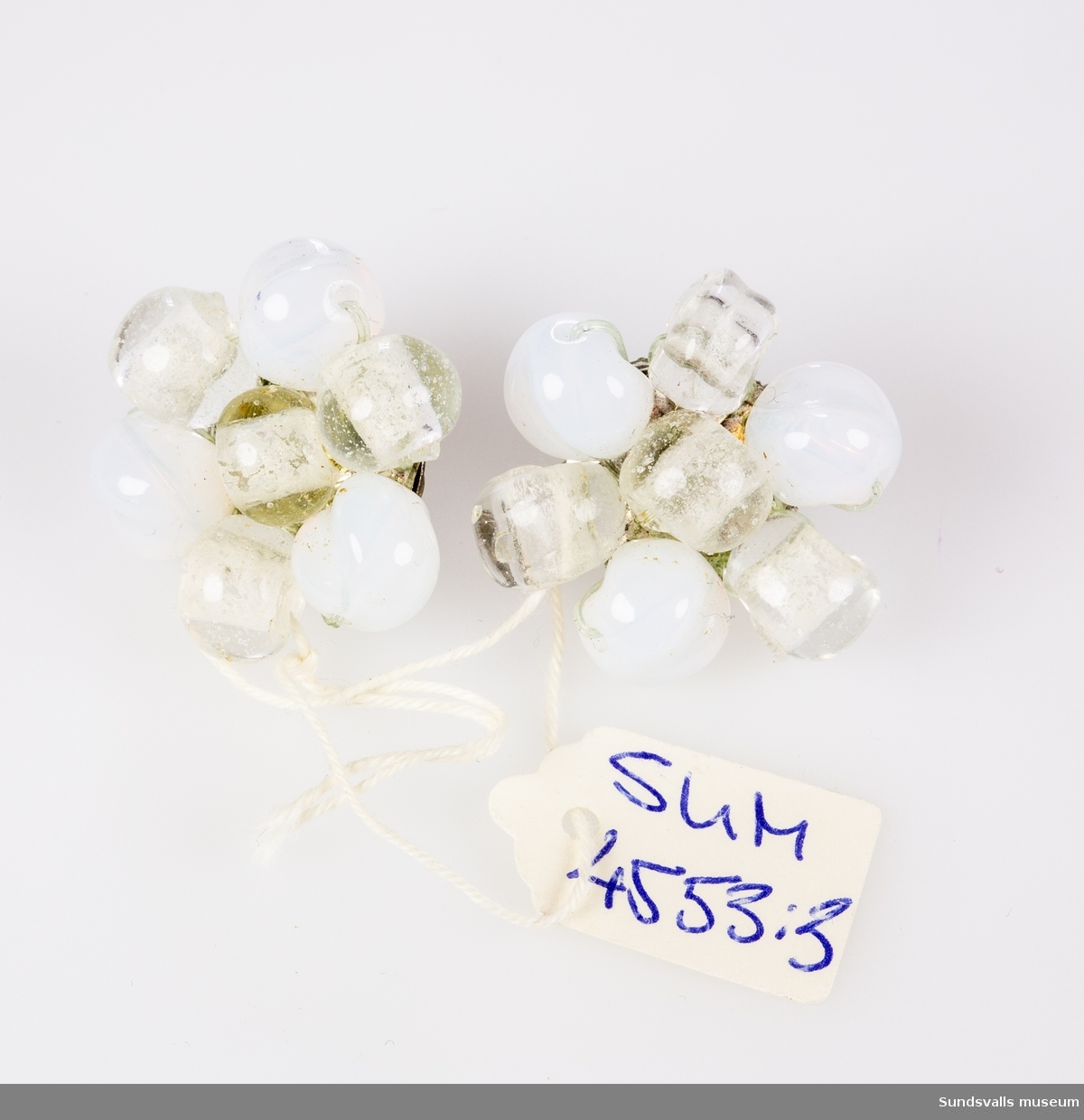 Ett par örhängen i clipsmodell. På clipset är sju ofärgade och vita pärlor fastsatta med nylontråd. Diam 2,8 cm.