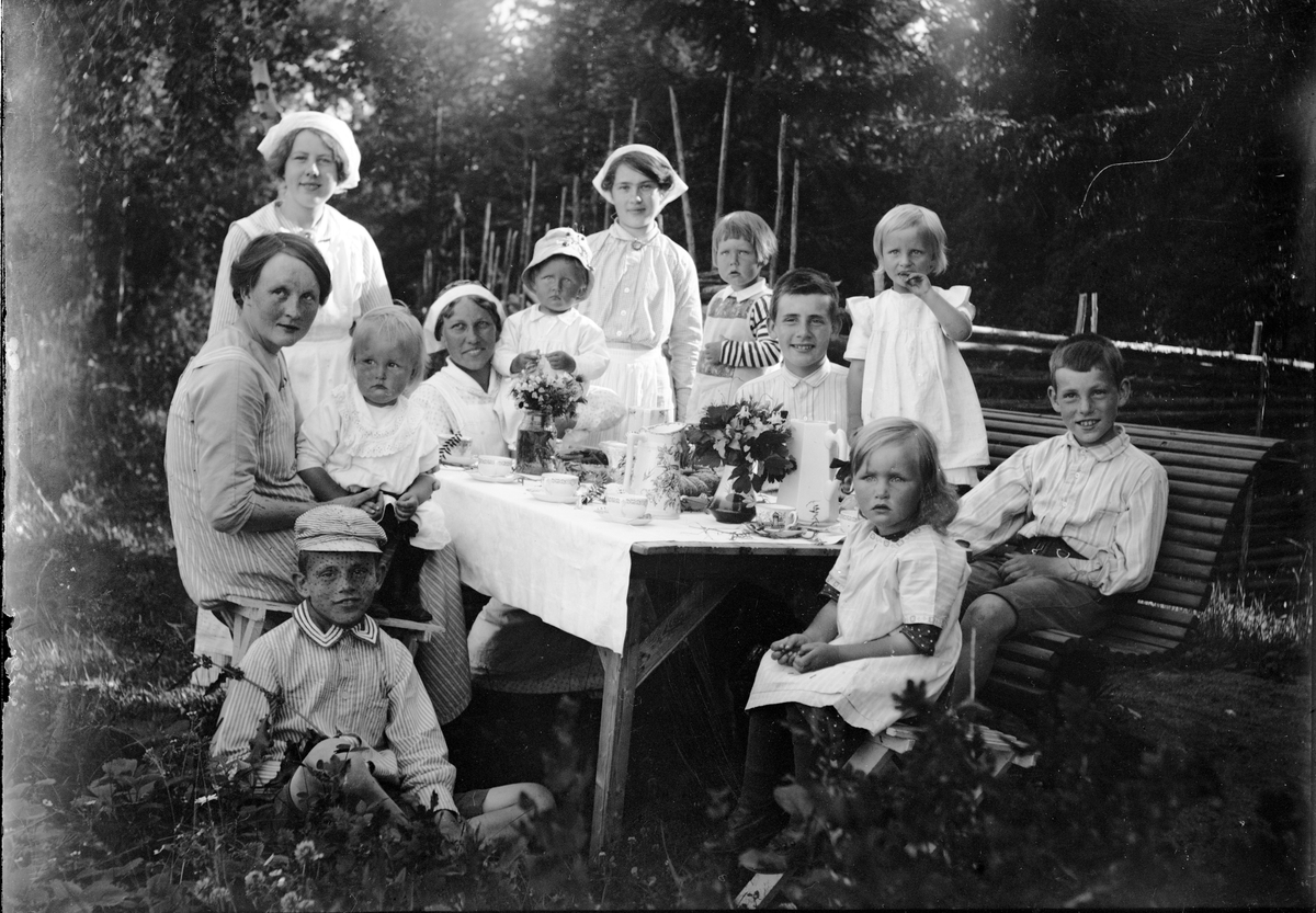 Christiane och Ruben Liljefors barn, Marit, Alf, Roland, Ingemar tillsammans med andra barn och hushållerskor vid kaffebord ute i trädgård, sannolikt Sverige