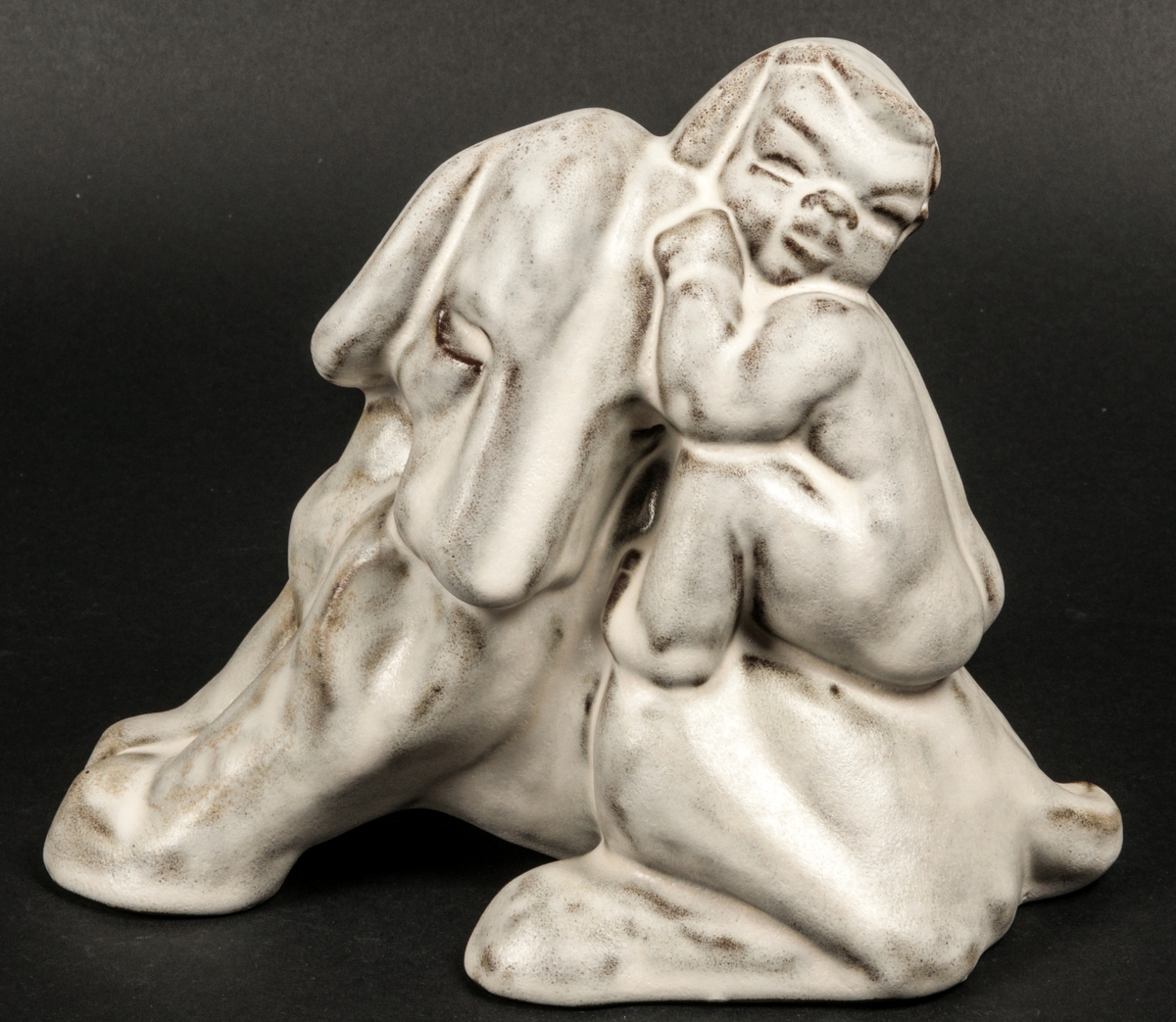 Figurin i stengods av Maggie Wibom, Gefle porslinsfabrik. Hund och pojke, 1933. Vit opak glasyr.